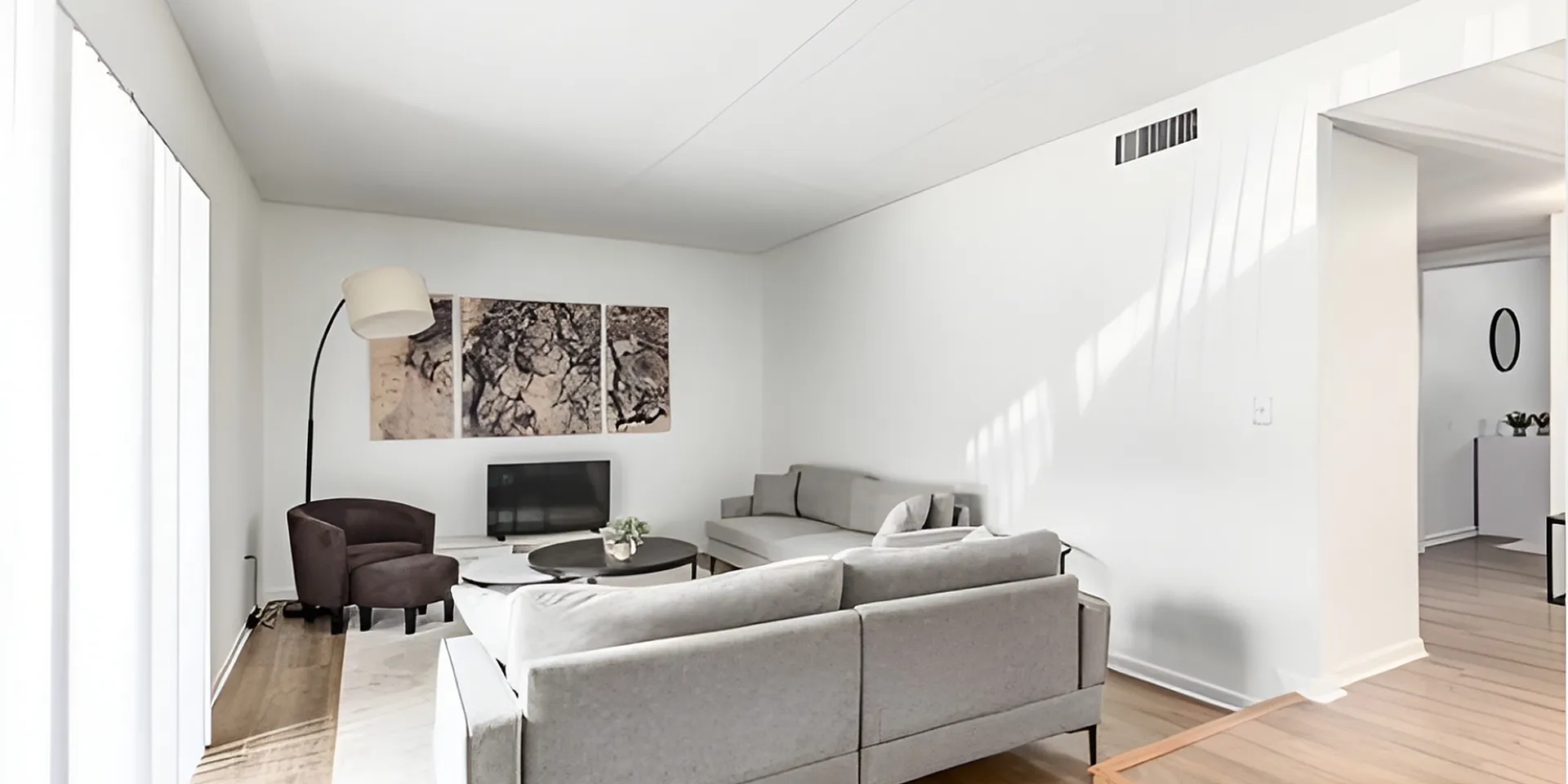 Bright and modern living room with sleek gray sofas, stylish floor lamp, and elegant wood flooring, perfect for relaxation and entertaining.
