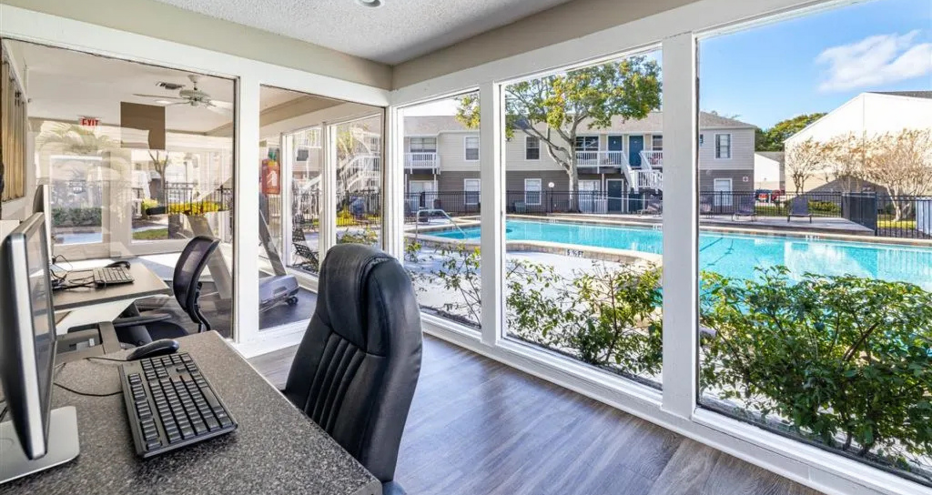 Bright office space with modern computers and panoramic pool view through large windows.