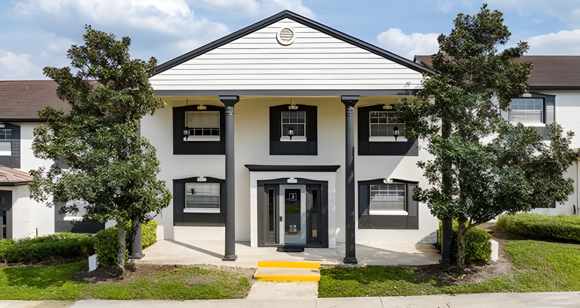 Elegant two-story building with grand entrance, classic columns, and lush greenery under a bright blue sky.