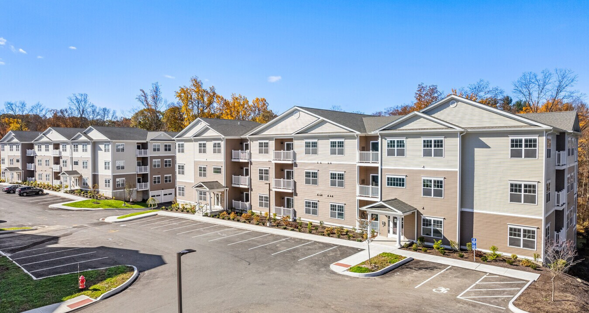 Elegant apartment complex with a modern design, featuring spacious balconies and ample parking, set against a backdrop of autumn trees.