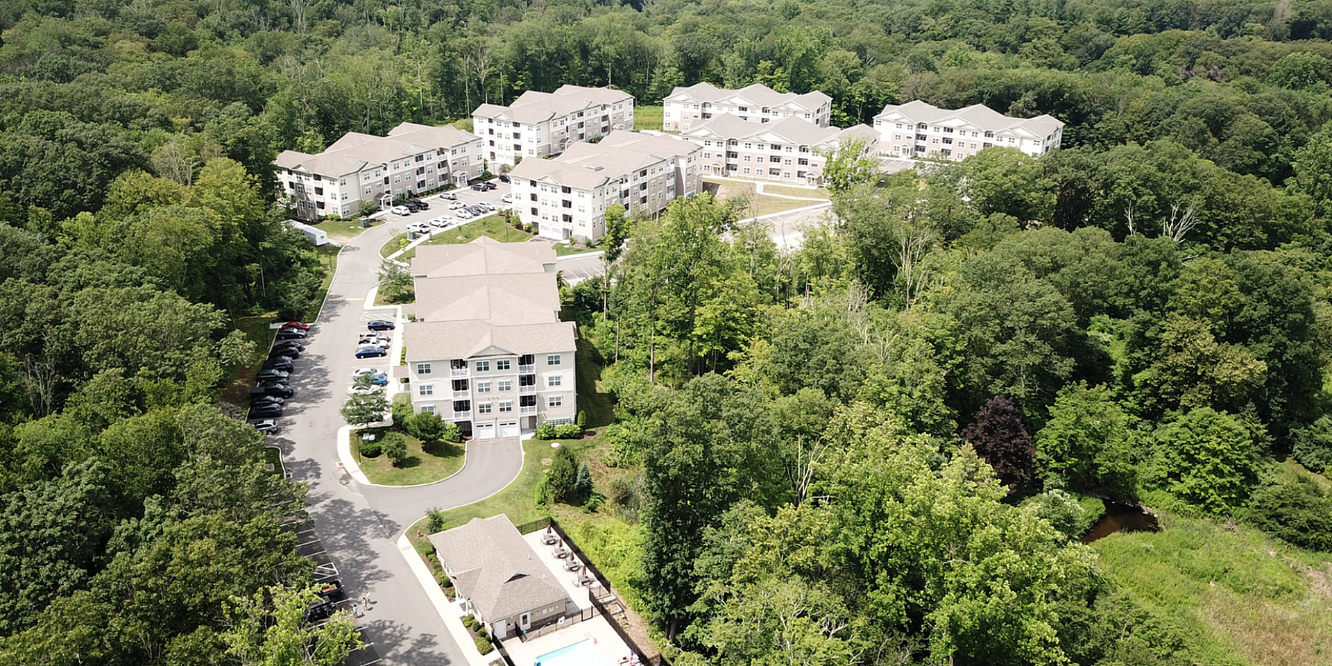 Enchanting aerial view of modern apartment complex nestled among lush greenery, featuring multiple buildings and a stunning outdoor pool area.