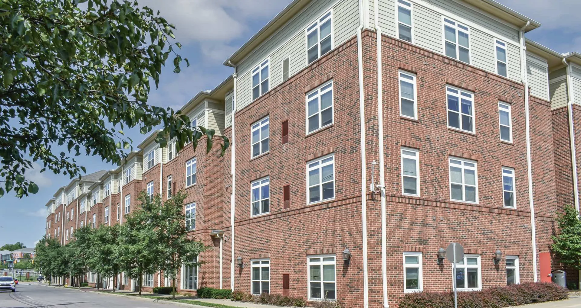 Charming brick apartment building with modern windows and lush greenery, offering a warm and inviting street view.
