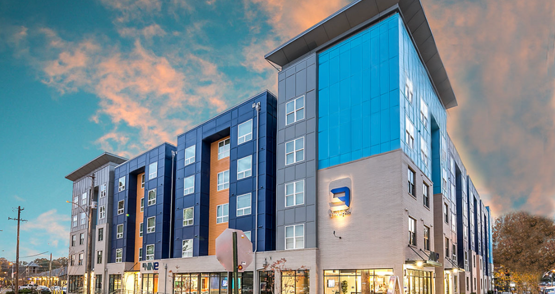 Modern apartment building with sleek blue and gray facade under a vibrant sky, offering urban living with style and convenience.