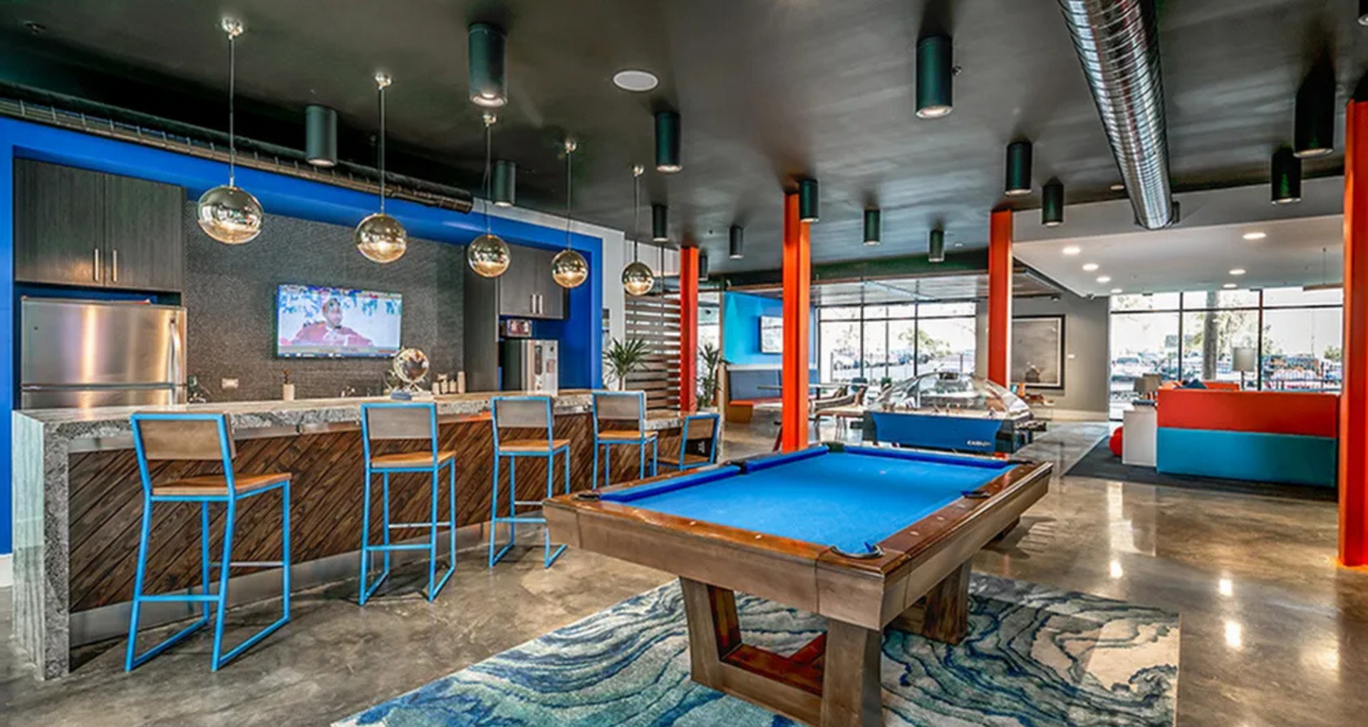 Chic and modern recreation area featuring a sleek bar with vibrant stools, stylish pool table, and cozy lounge space for entertainment.
