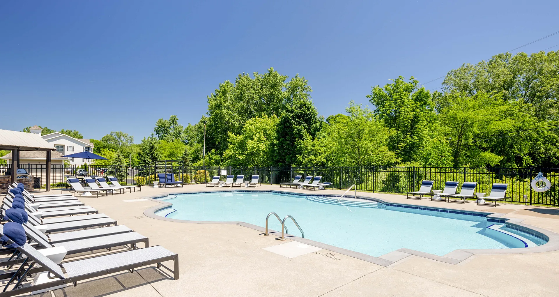 Inviting outdoor pool area with stylish lounge chairs, surrounded by lush greenery and a clear blue sky.