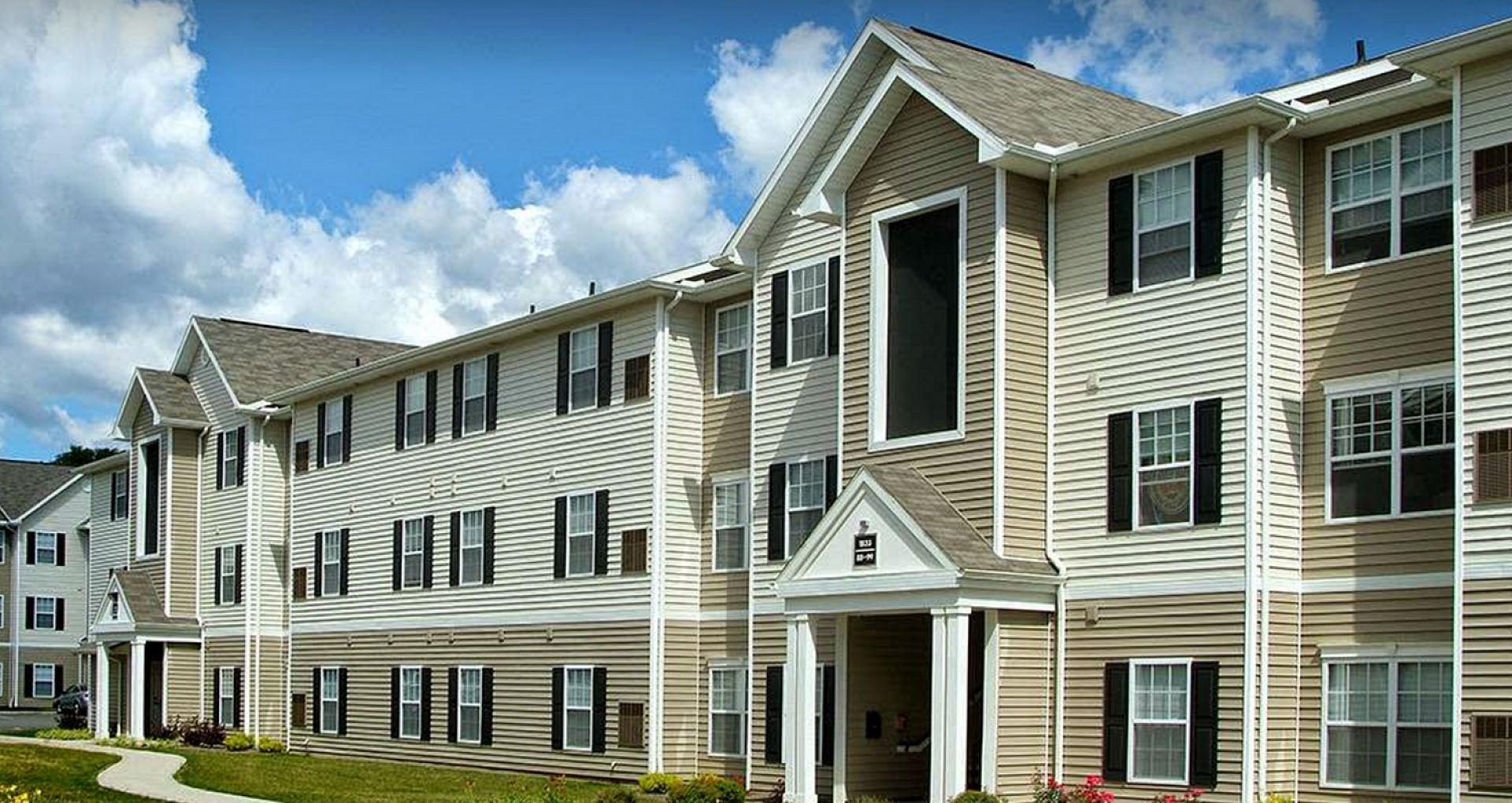 Charming apartment complex with traditional architectural design, surrounded by well-maintained lawns and a clear blue sky.