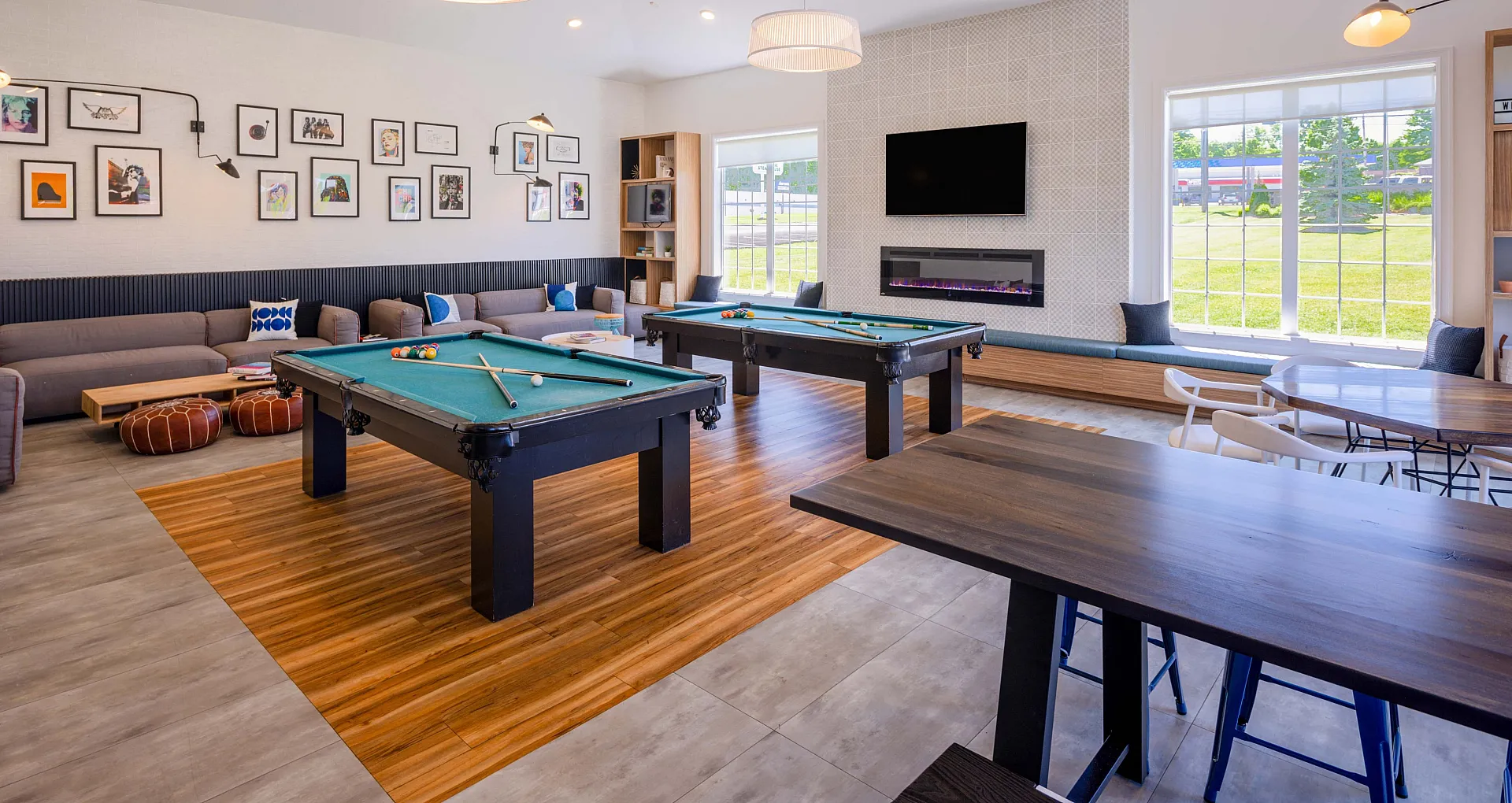 Contemporary recreational room featuring dual pool tables, cozy lounge seating, stylish wall art, and abundant natural light, perfect for entertainment and relaxation.