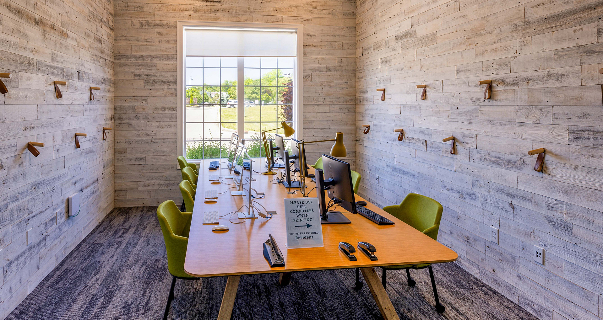 Bright and inviting workspace with a modern communal table, sleek computers, and chic green chairs, perfect for productivity and collaboration.