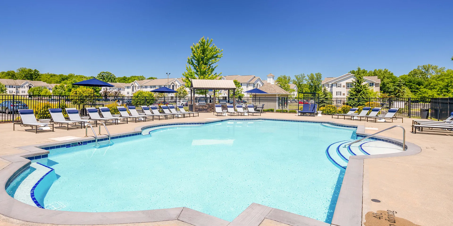 Inviting outdoor pool area with sun loungers, surrounded by lush greenery and modern apartments, perfect for relaxation and leisure.