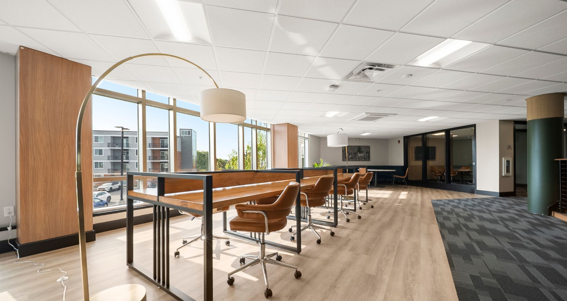 Bright and modern communal workspace with large windows, stylish wooden desks, and comfortable swivel chairs offering a productive environment.
