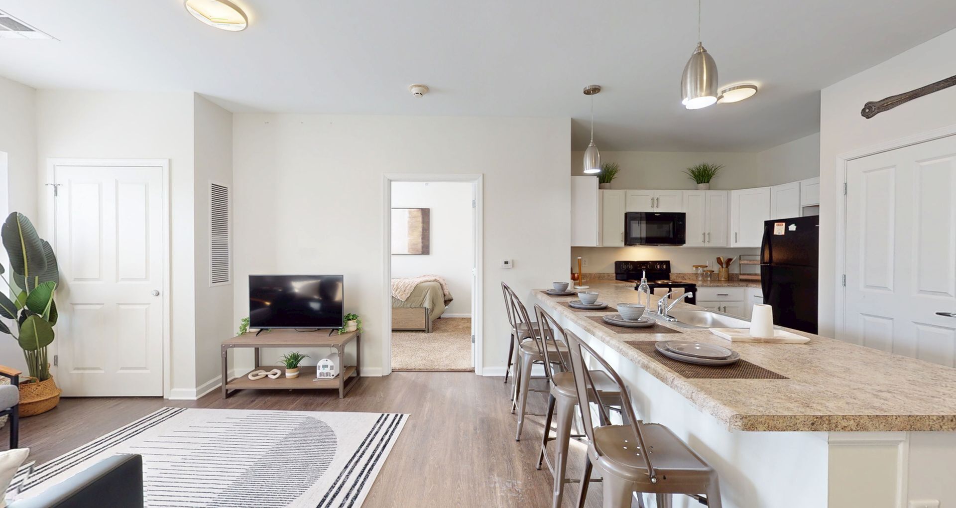 Inviting open-layout apartment with modern kitchen, cozy living area, and a warm-toned bedroom visible in the background.