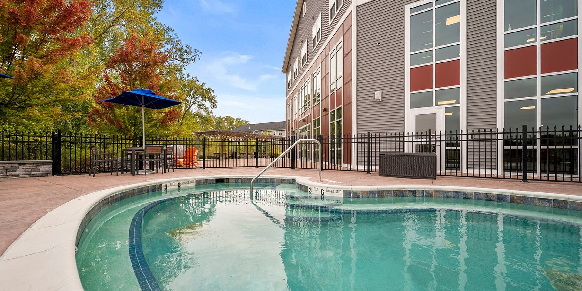 Inviting outdoor pool area with vibrant umbrellas and lush greenery, perfect for relaxation beside a modern apartment complex.