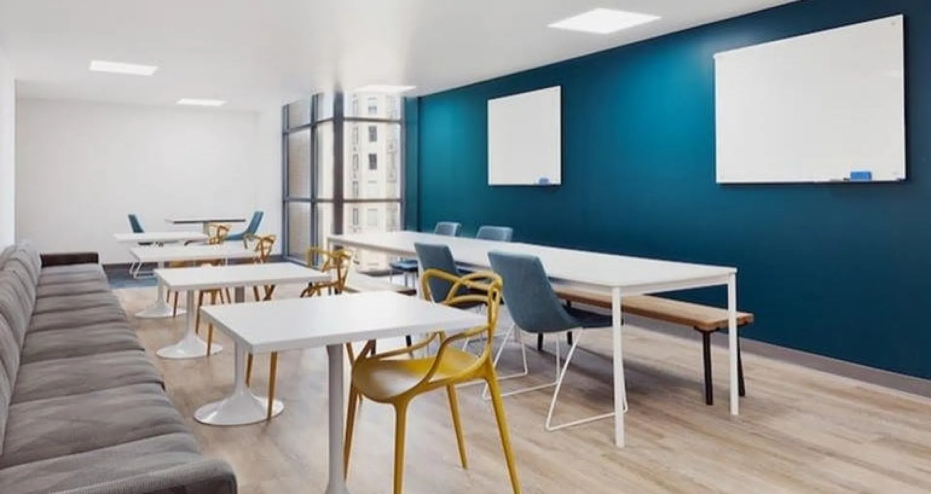 Modern communal workspace with sleek tables, vibrant chairs, and a stylish blue accent wall, offering a bright and inviting environment for collaboration.