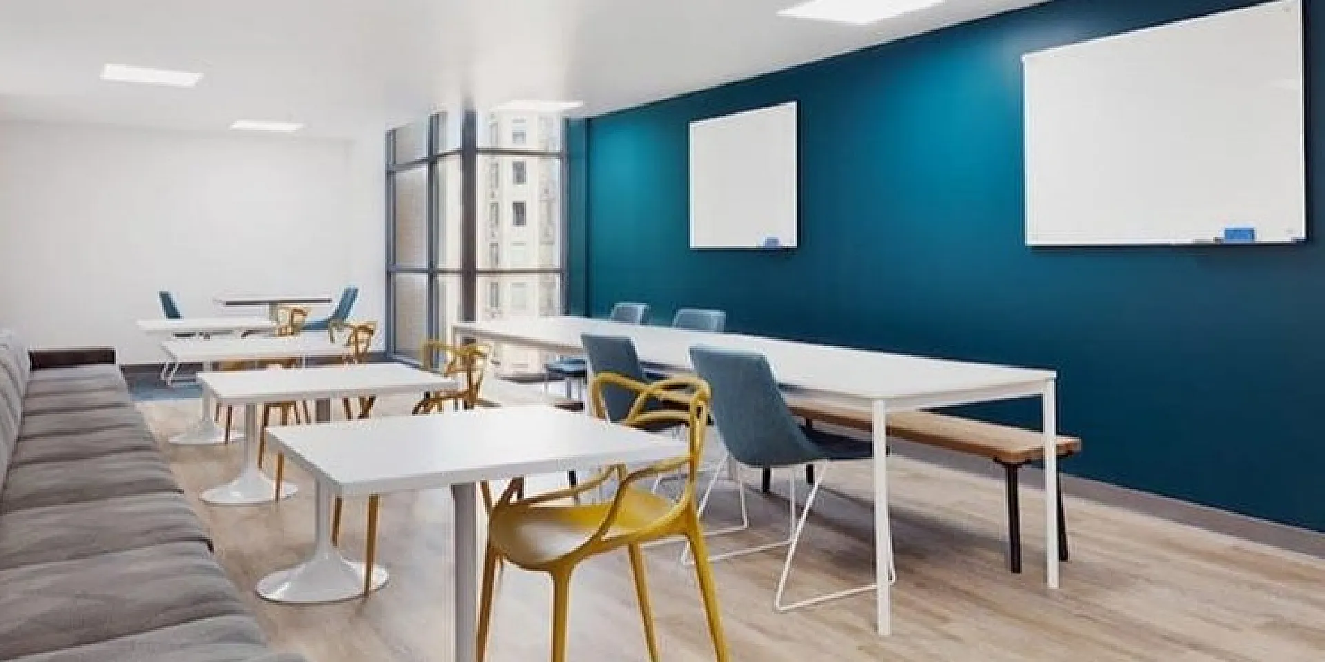 Modern co-working space with sleek tables, vibrant chairs, and large windows providing natural light.