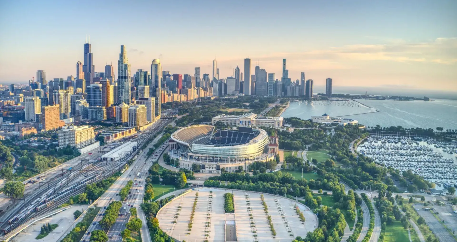 Stunning aerial view of a vibrant city skyline, featuring lush parks, a famous stadium, and a sparkling waterfront at sunset.