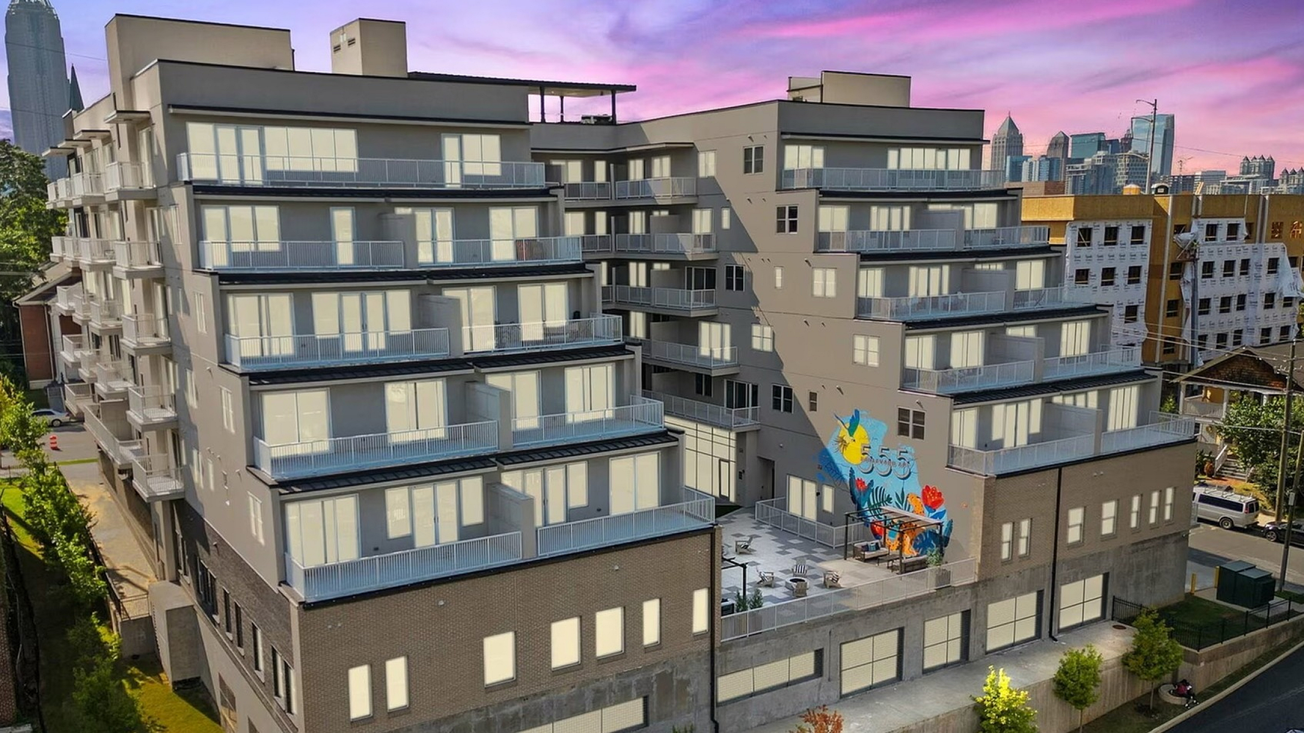 Modern apartment building with multiple balconies offering stunning sunset views of the city skyline, featuring vibrant street art on the exterior.