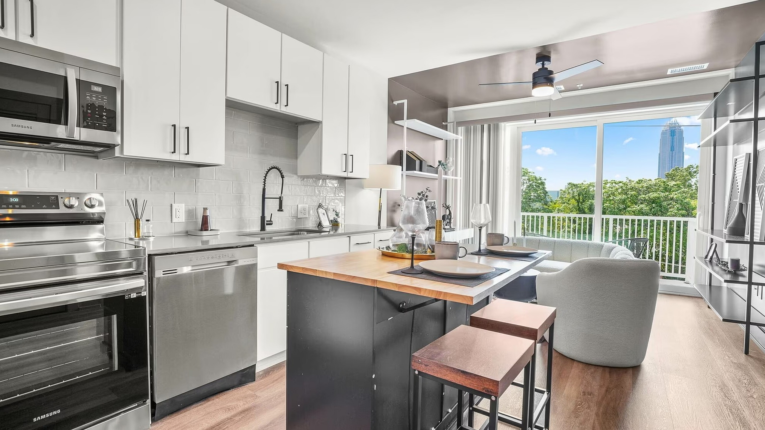 Modern kitchen and living space with sleek white cabinetry, stainless steel appliances, and a bright open layout featuring a stunning city view through large windows.
