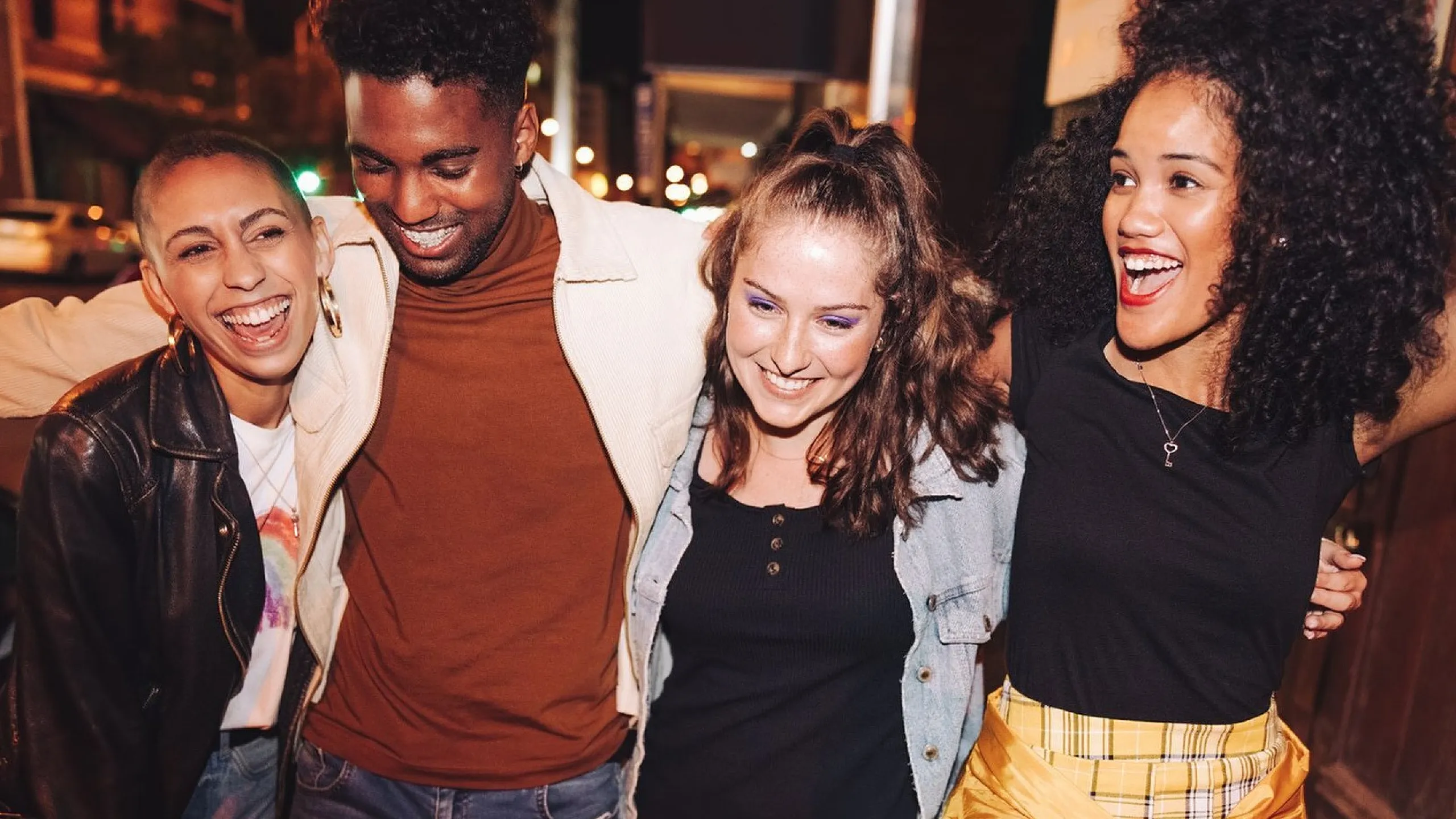 Group of friends joyfully laughing and embracing each other during a vibrant night out in the city.