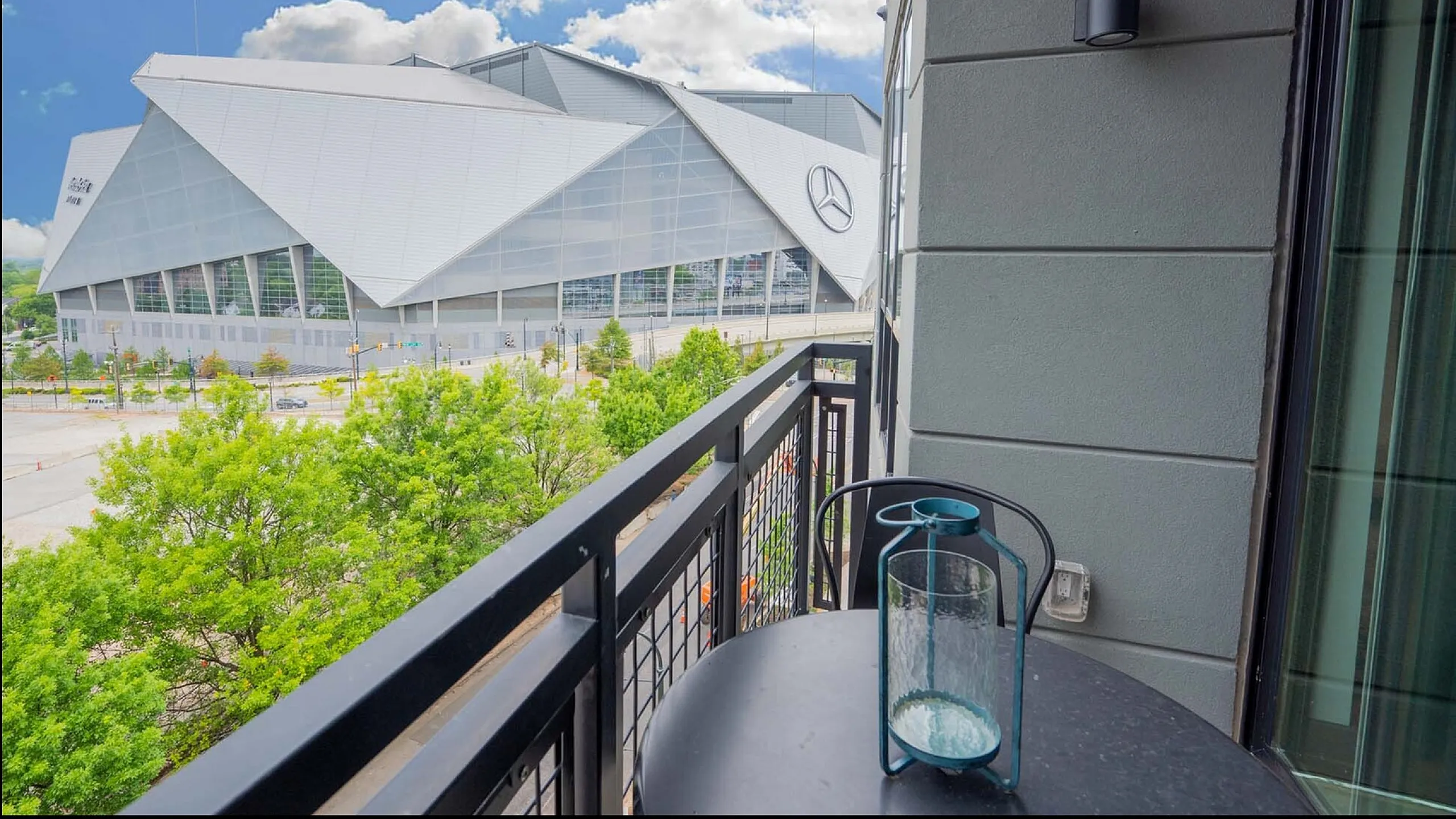Chic apartment balcony offering a stunning view of a modern stadium under a bright blue sky.