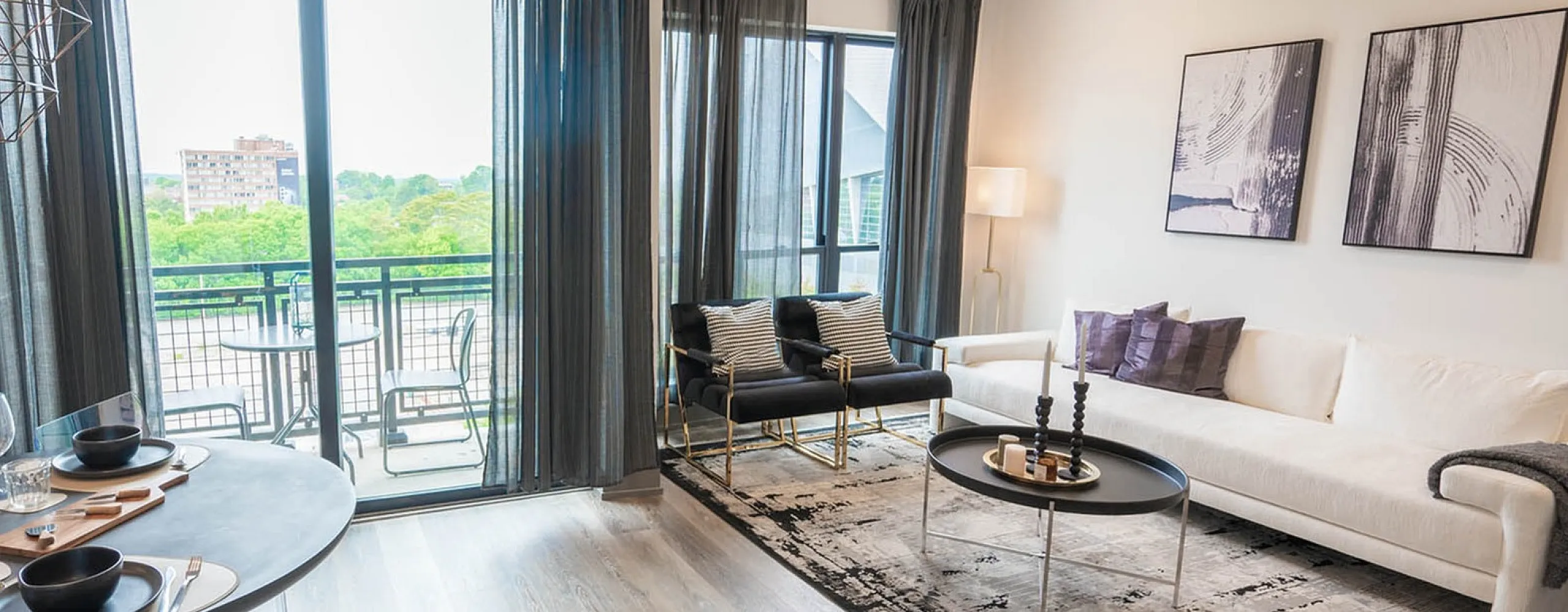 Contemporary open-concept living area with modern furnishings, floor-to-ceiling windows, and a stylish dining setup leading to a scenic balcony.