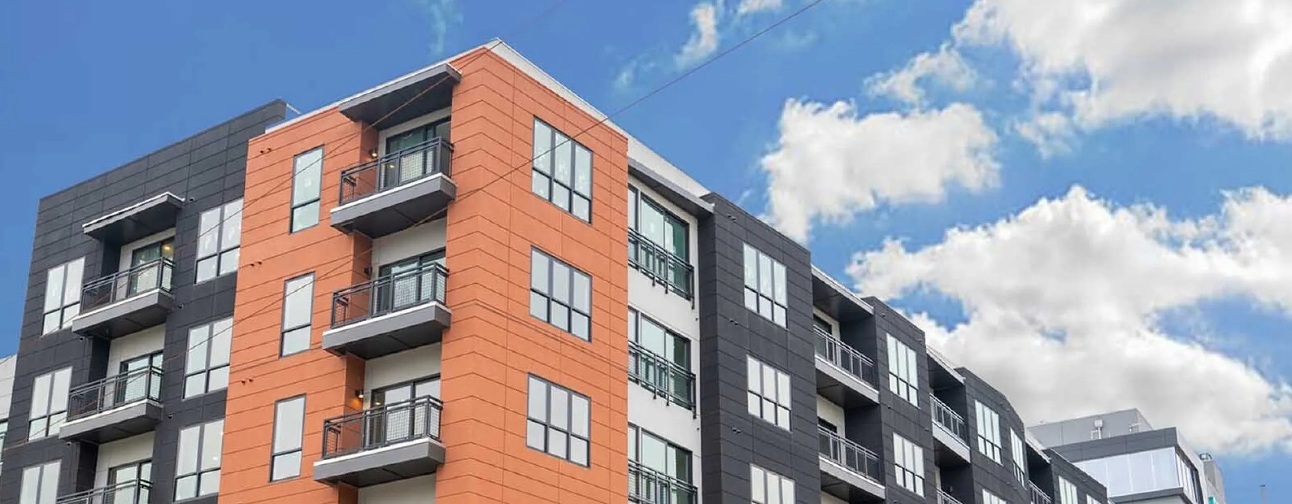 Contemporary urban apartment complex with vibrant facade, featuring multiple private balconies and lush street landscaping.
