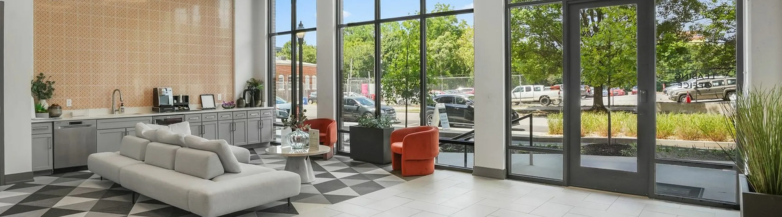 Modern lobby interior with geometric flooring, stylish grey seating, vibrant red chairs, and expansive windows offering a scenic outdoor view.