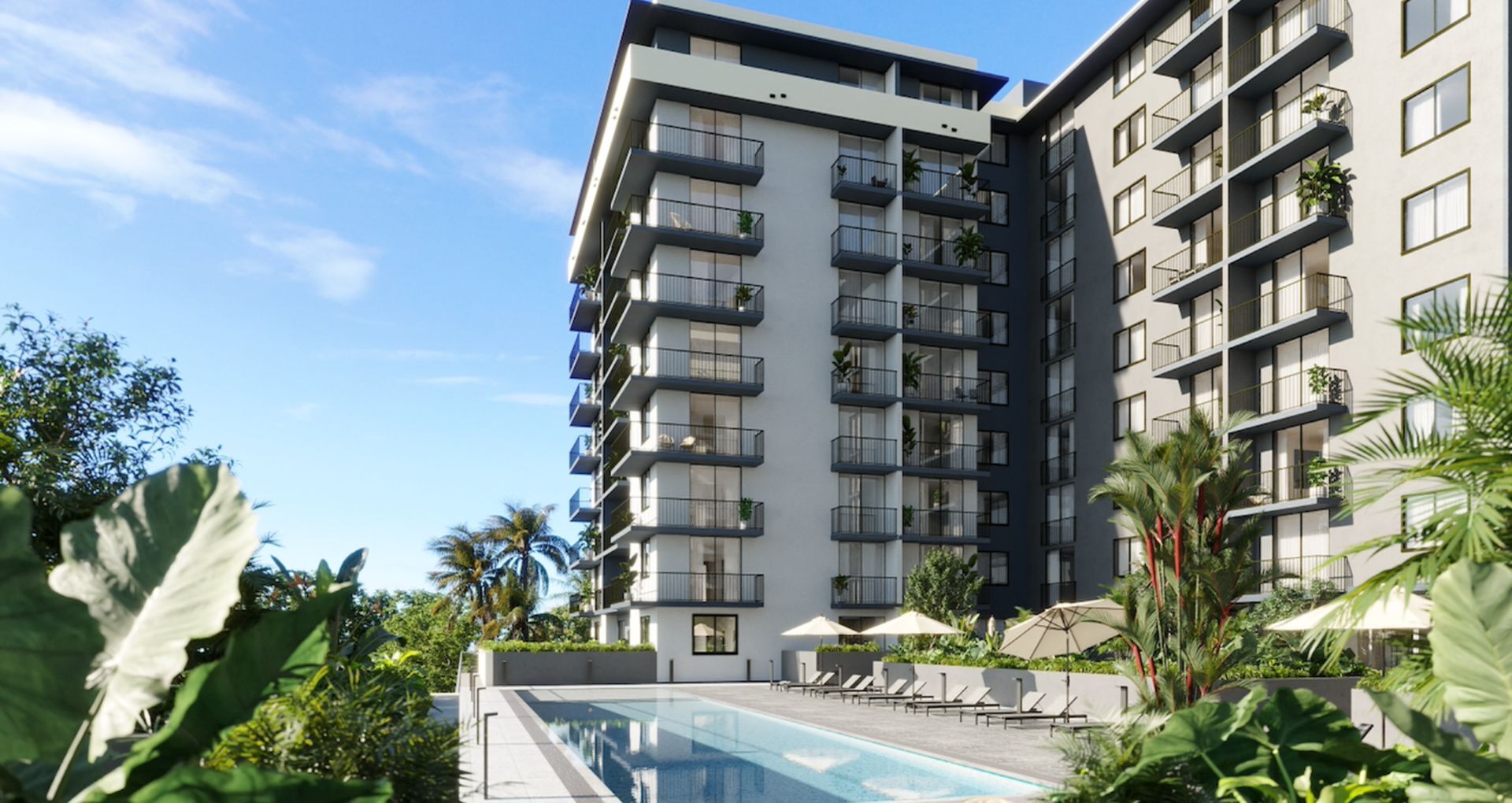 Modern apartment complex with beautiful balconies overlooking a lush garden and a sparkling swimming pool, surrounded by ample greenery under a clear blue sky.