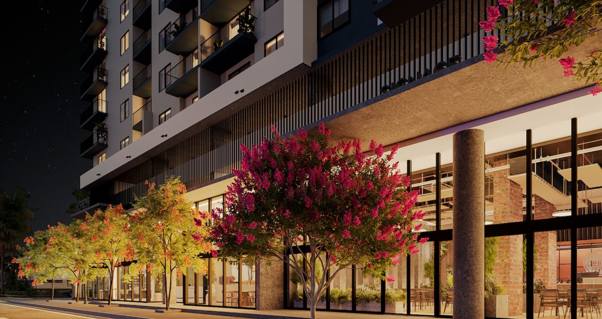Elegant modern apartment building with vibrant pink flowers and illuminated facade at night.