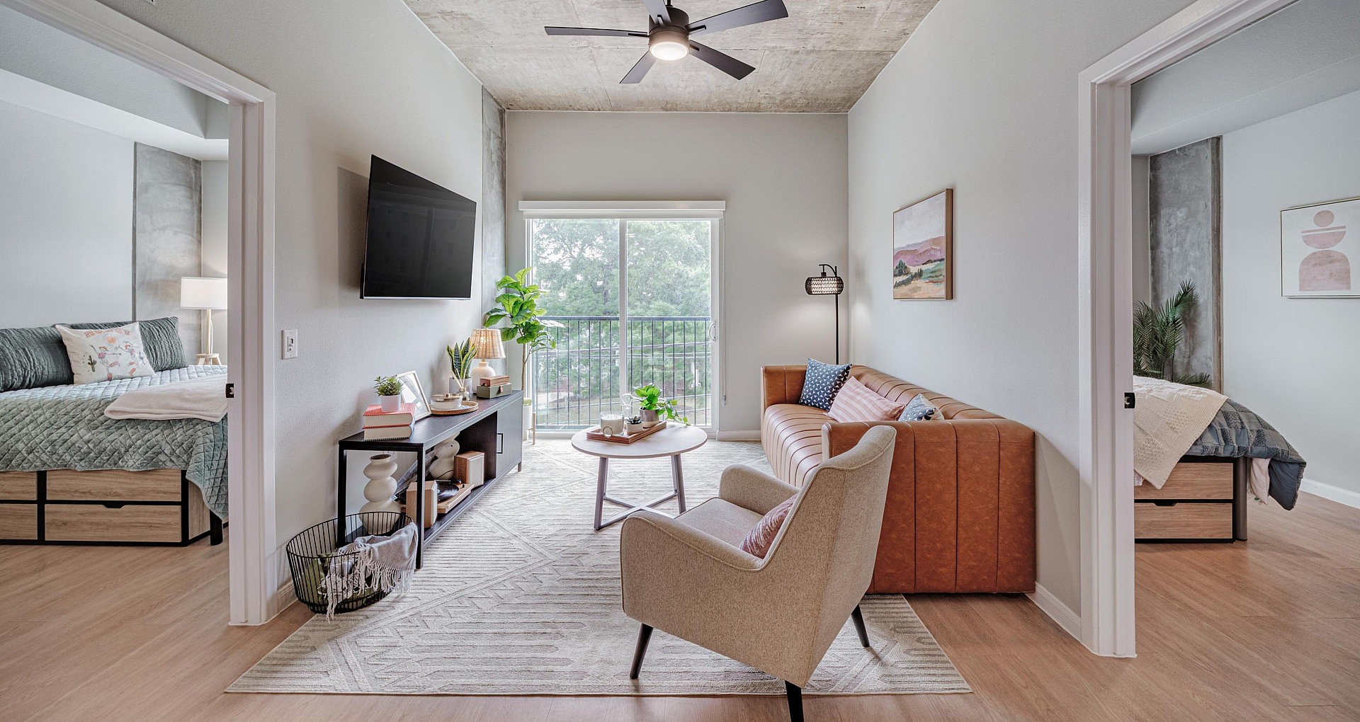Bright and inviting living room with modern decor, featuring a cozy sofa, elegant armchair, wall-mounted TV, and natural light streaming through large glass doors.