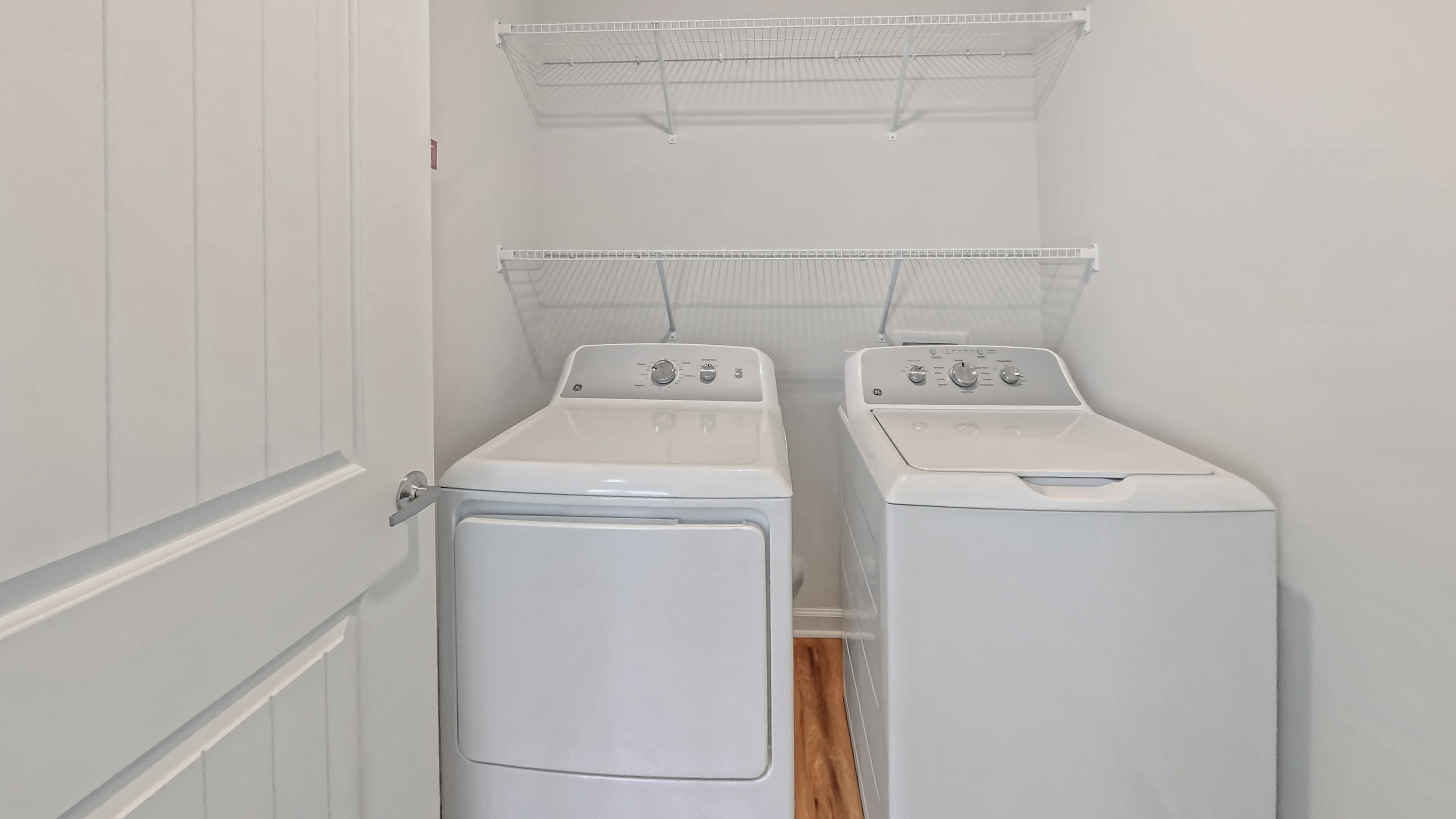 Modern laundry room featuring sleek white washer and dryer with overhead shelving for storage.
