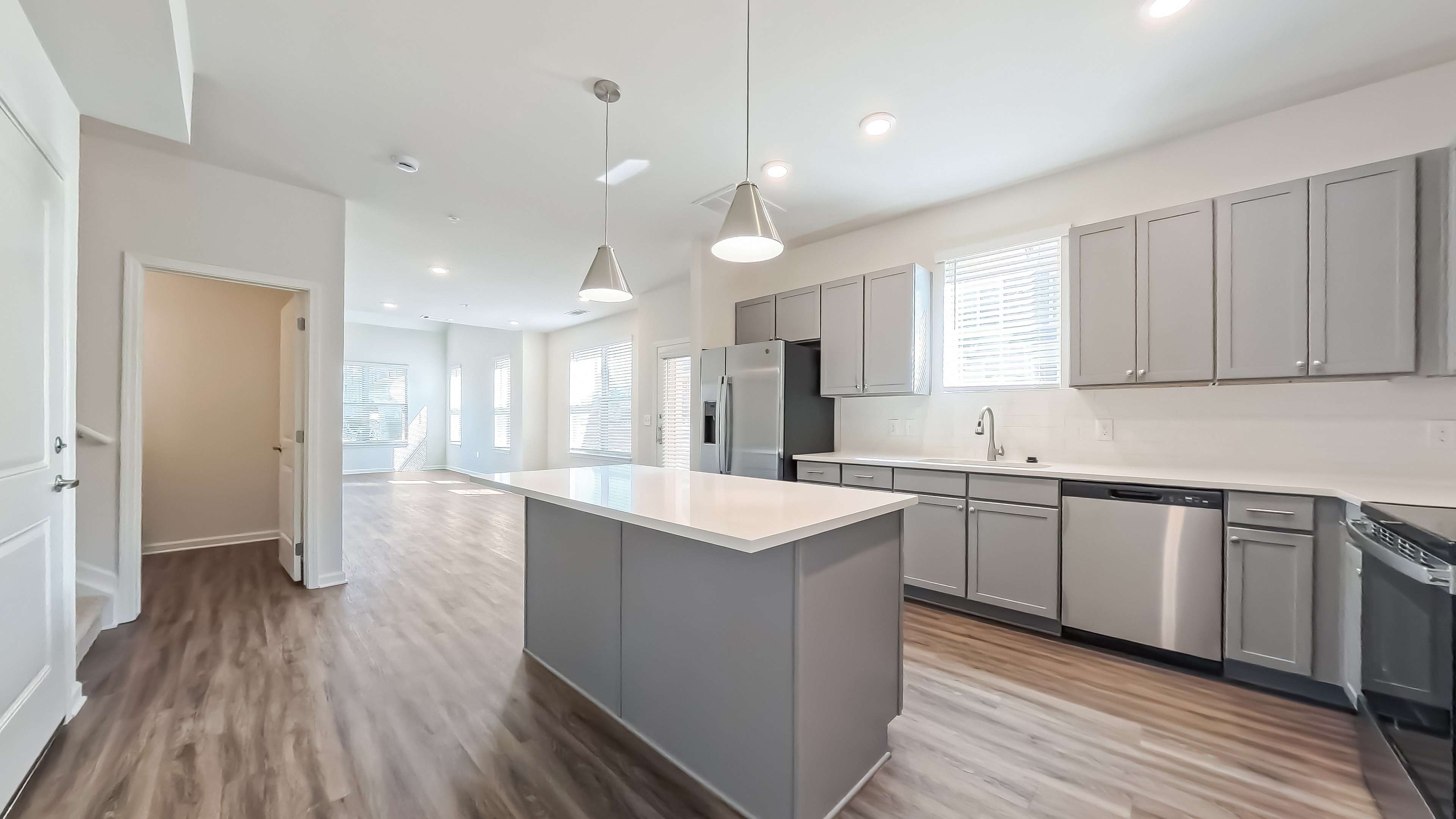 Modern kitchen with sleek gray cabinetry, stainless steel appliances, and a spacious island, flowing into an open-concept living area with abundant natural light.