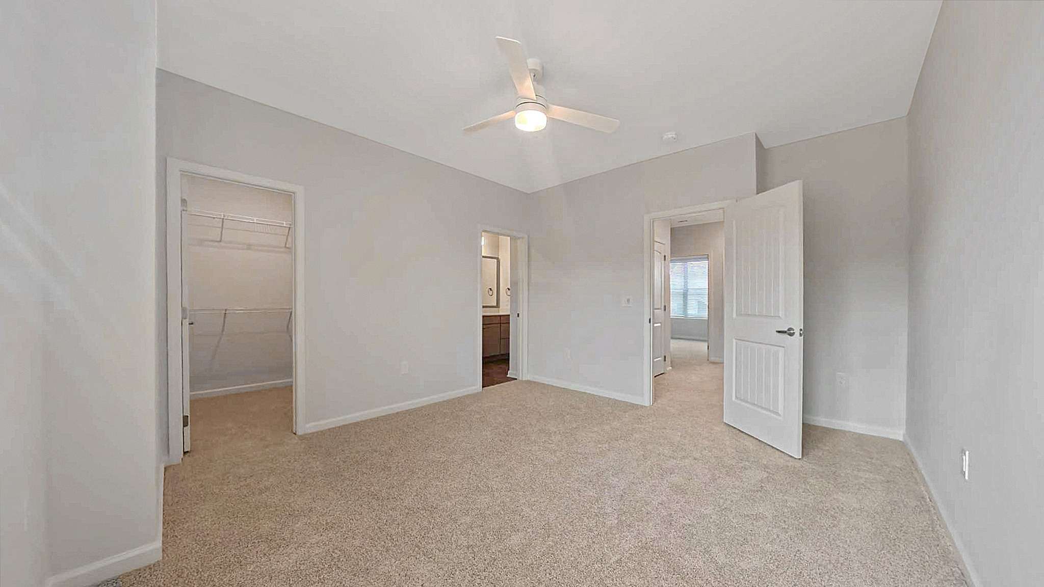 Bright, spacious bedroom with plush carpet, ceiling fan, and walk-in closet, exuding modern comfort and style.
