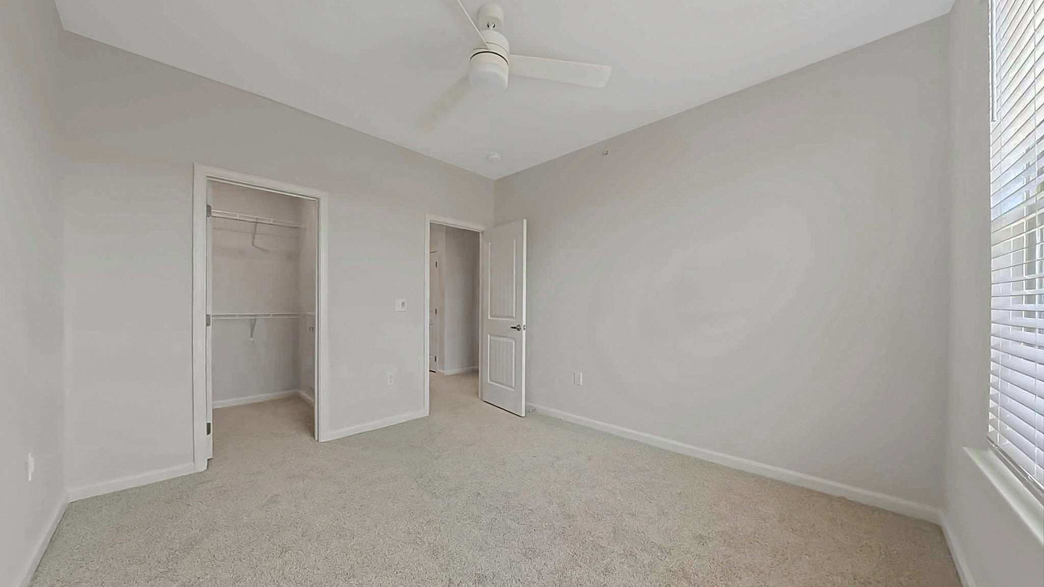 Bright and airy bedroom with plush carpet, neutral walls, and a ceiling fan, featuring a spacious walk-in closet.