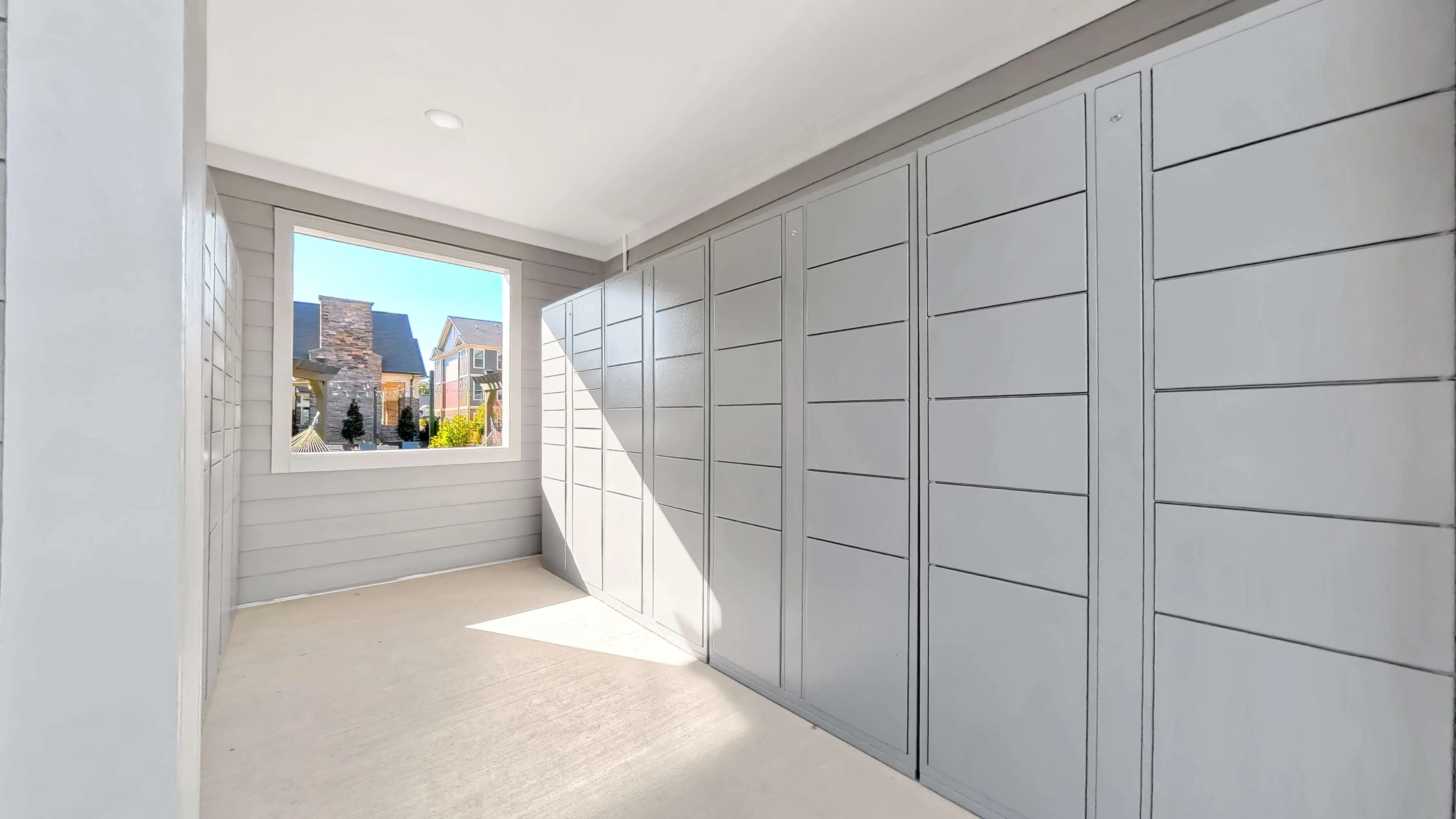 Modern apartment storage area with sleek gray cabinets and a bright window view of a charming neighborhood.