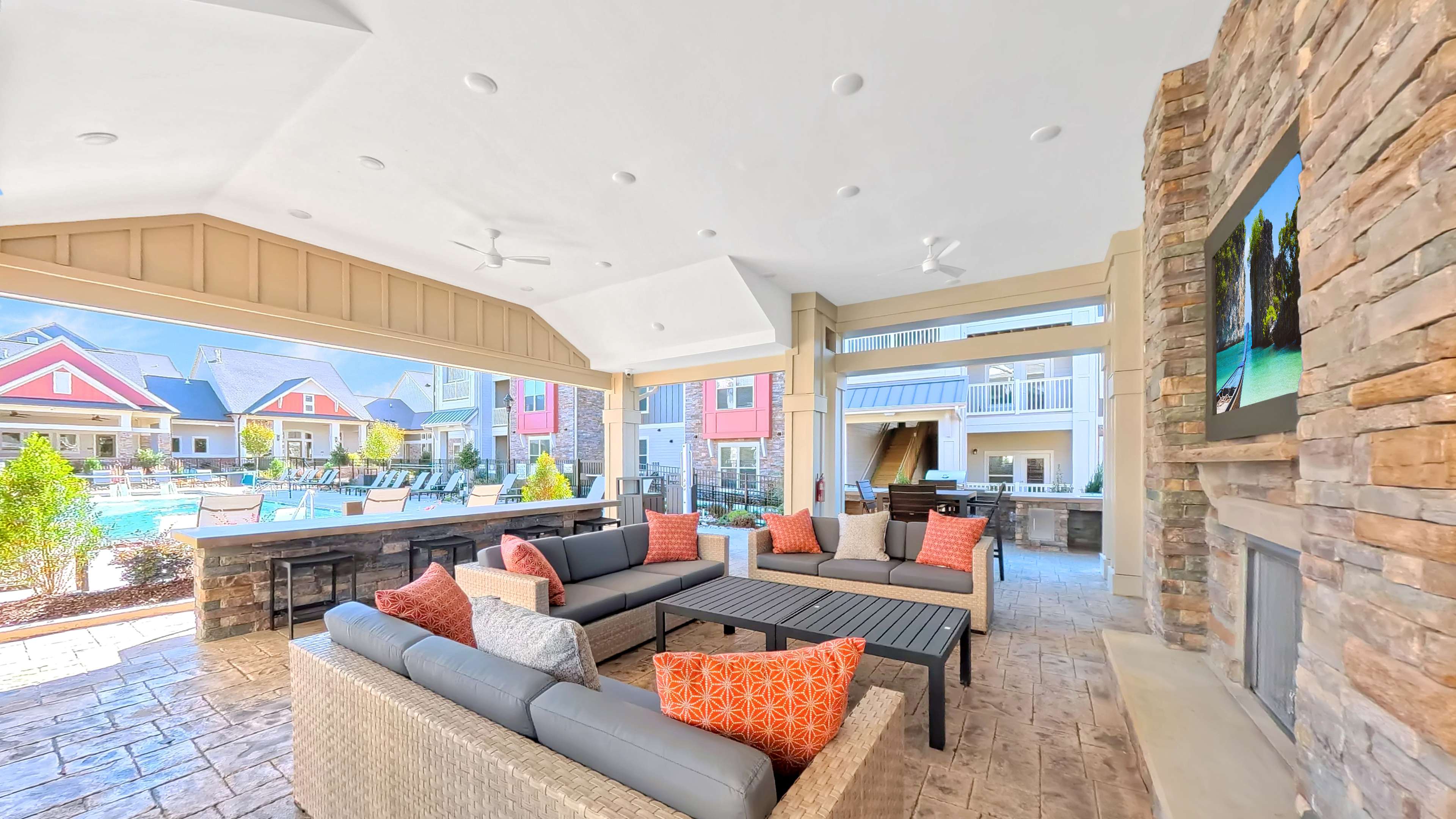 Luxury outdoor lounge area with stylish seating and vibrant cushions, overlooking a sparkling pool and charming apartment buildings.