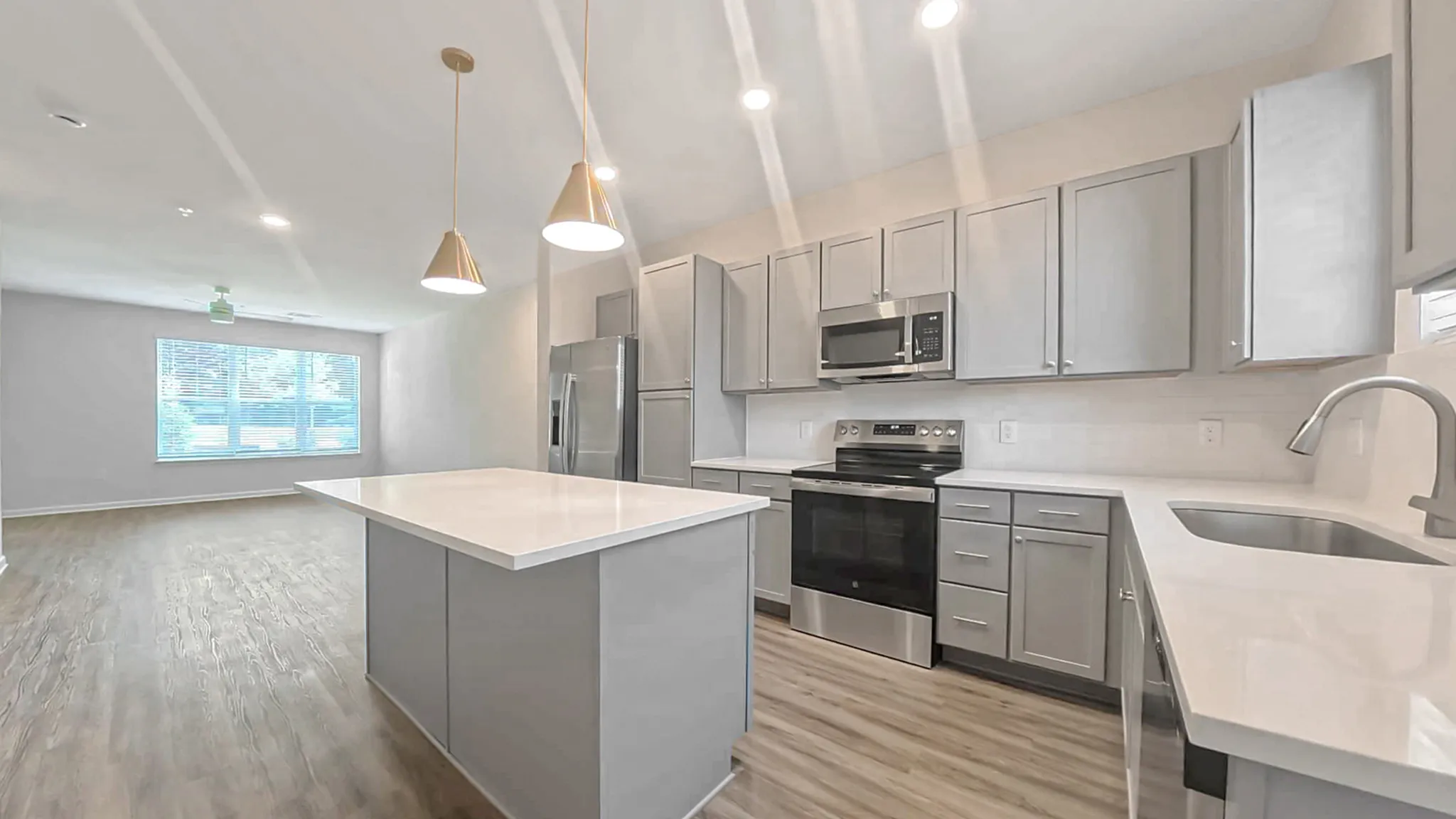 Modern kitchen with sleek cabinetry, stainless steel appliances, and a spacious island under elegant pendant lighting, overlooks open living area with large windows.