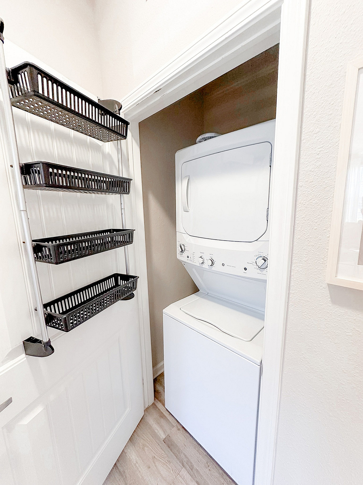 Compact laundry nook with a sleek white stacked washer and dryer, featuring convenient over-door storage racks.