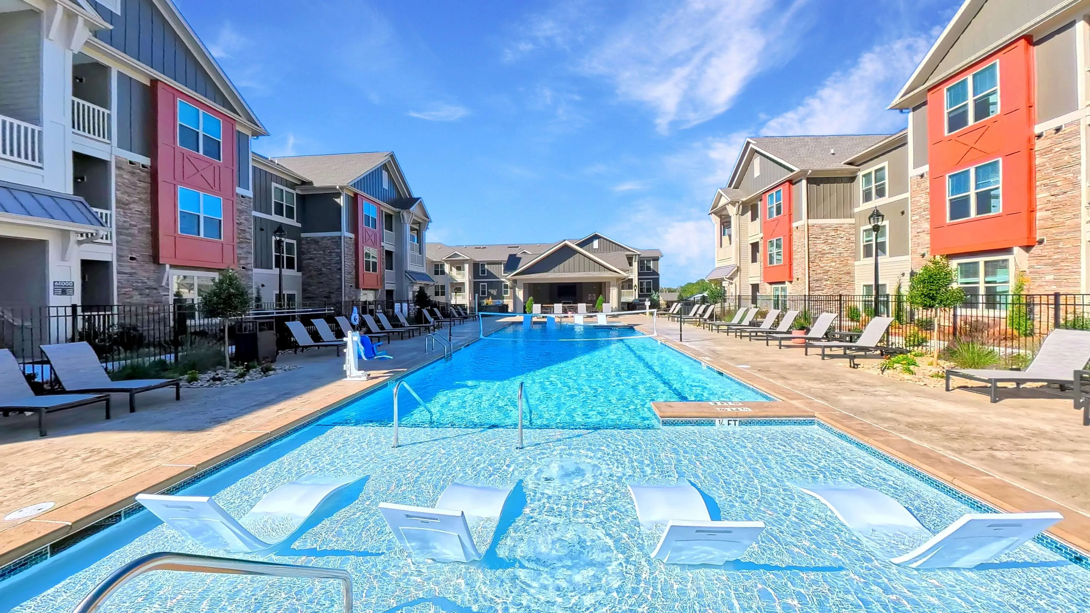 Luxurious apartment complex with a crystal-clear pool, stylish lounge chairs, and modern architecture under a clear blue sky.