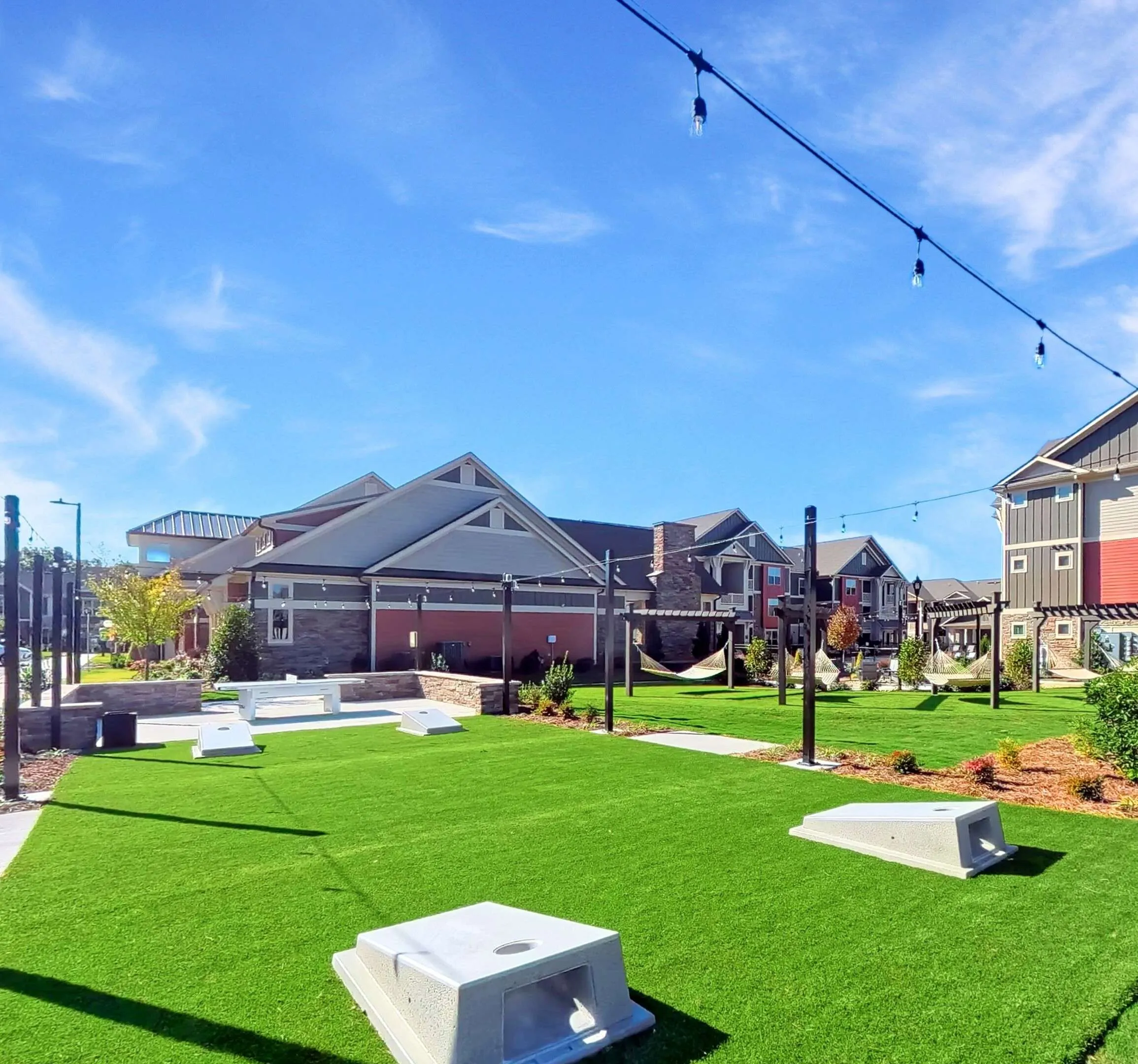 Charming outdoor recreational area with vibrant green lawn, modern lighting, cozy hammocks, and elegant townhouses under a clear blue sky.
