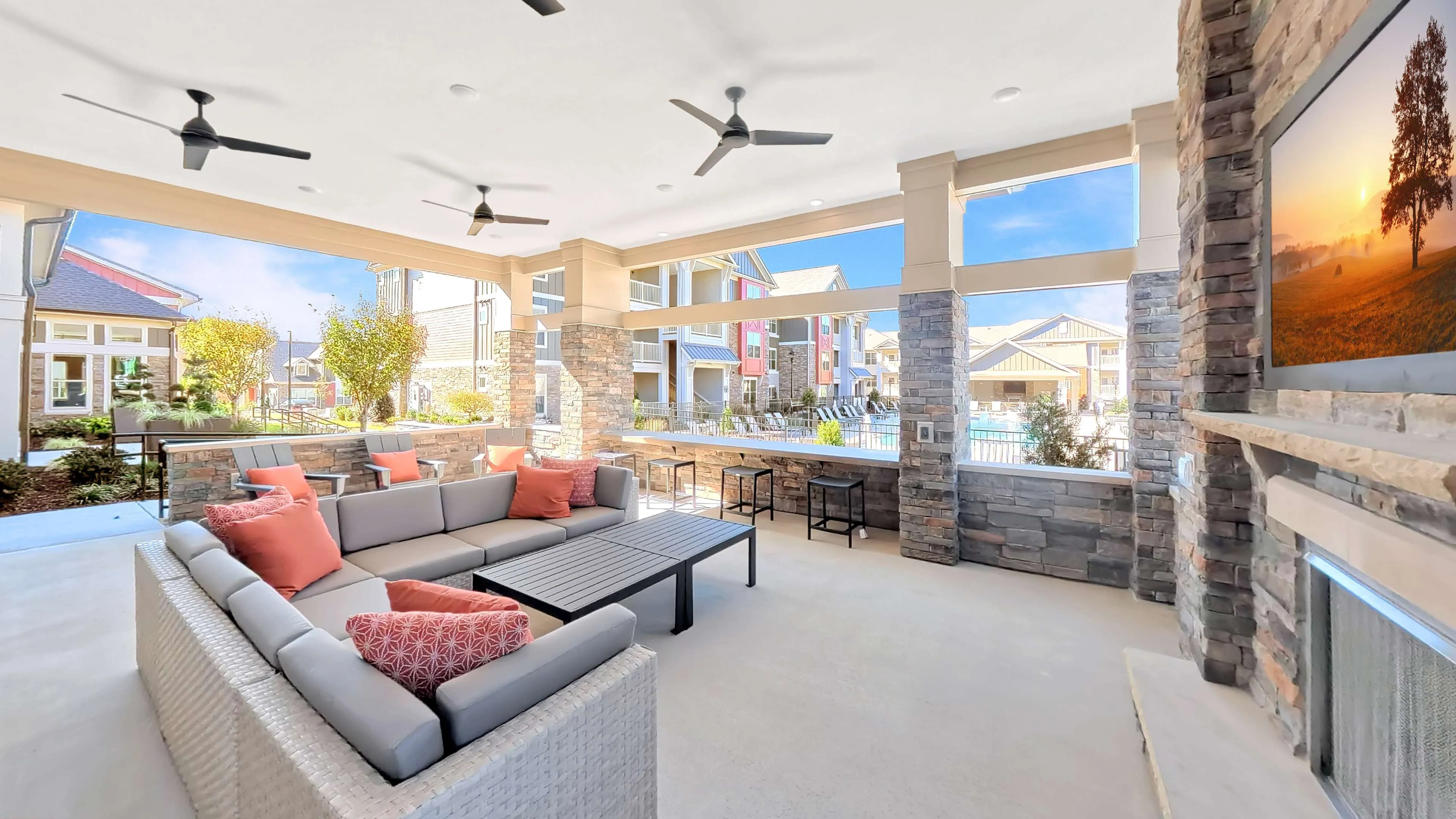 Inviting outdoor lounge area with cozy seating, modern ceiling fans, and scenic views of a vibrant apartment complex and pool.
