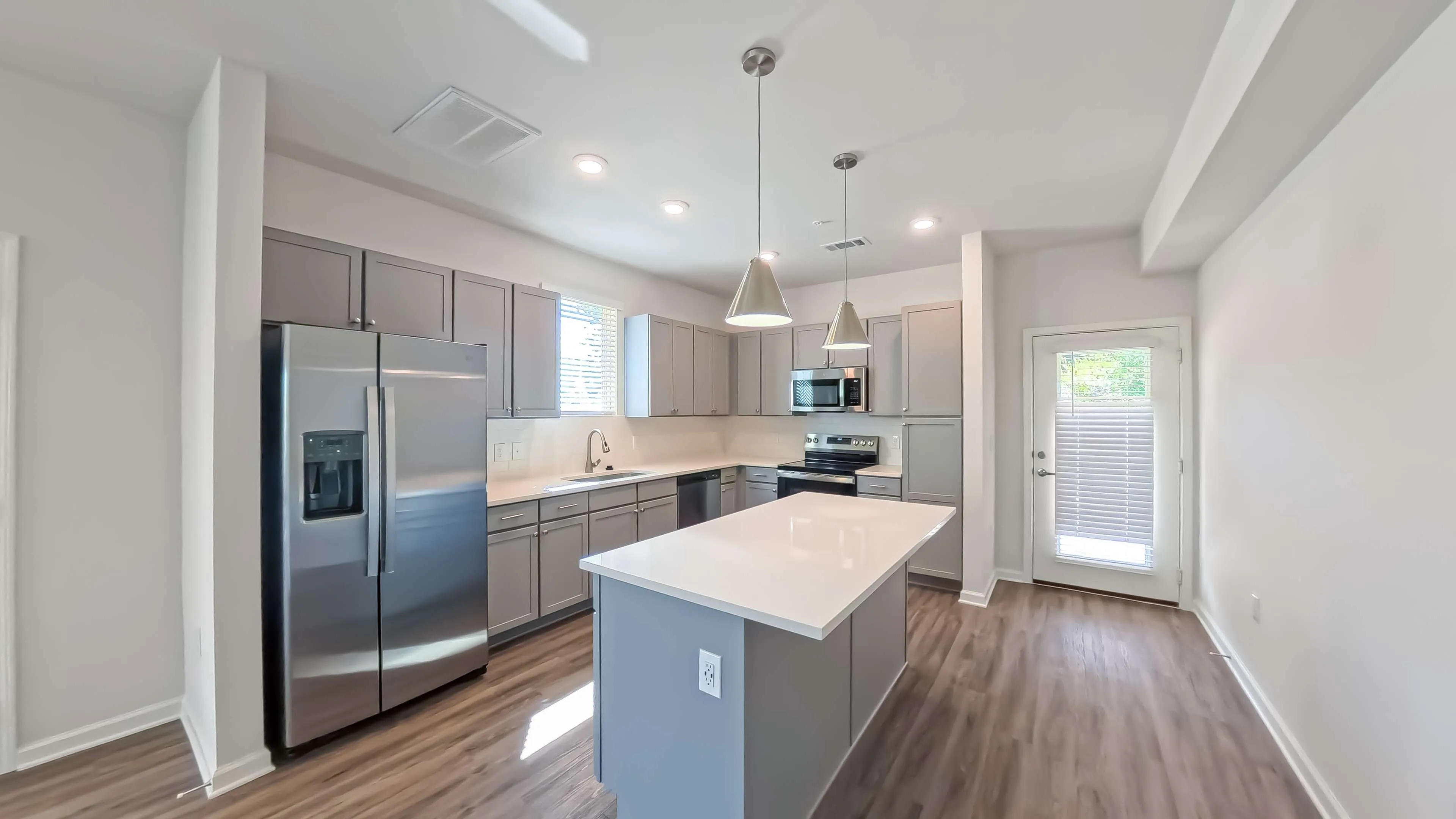 Modern kitchen with sleek gray cabinets, spacious island, stainless steel appliances, and elegant pendant lighting.