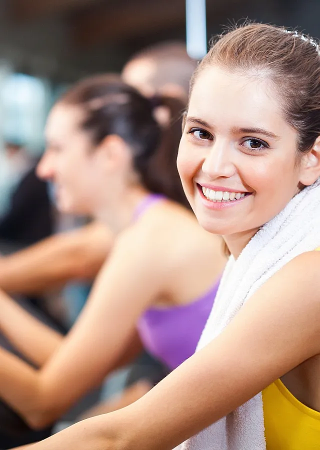 Vibrant gym scene with a smiling woman on an exercise bike, capturing the lively and energetic atmosphere of the fitness center.