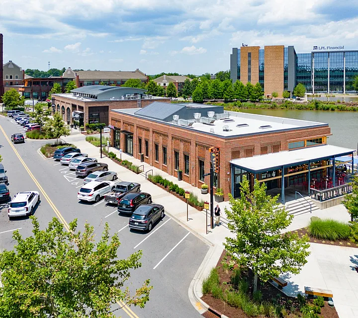 Charming urban scene with stylish brick buildings along a tree-lined street, featuring ample parking and a scenic waterfront view.