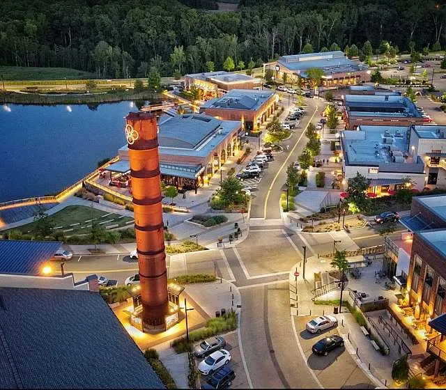 Vibrant aerial view of a lively shopping center with modern architecture, a central landmark tower, and scenic waterfront setting surrounded by lush greenery.