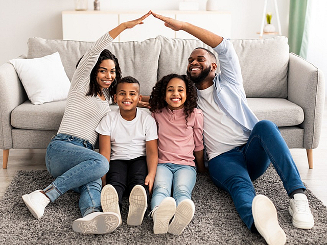 Happy family sitting in a bright, modern living room with a cozy gray sofa and stylish decor, exuding warmth and comfort.