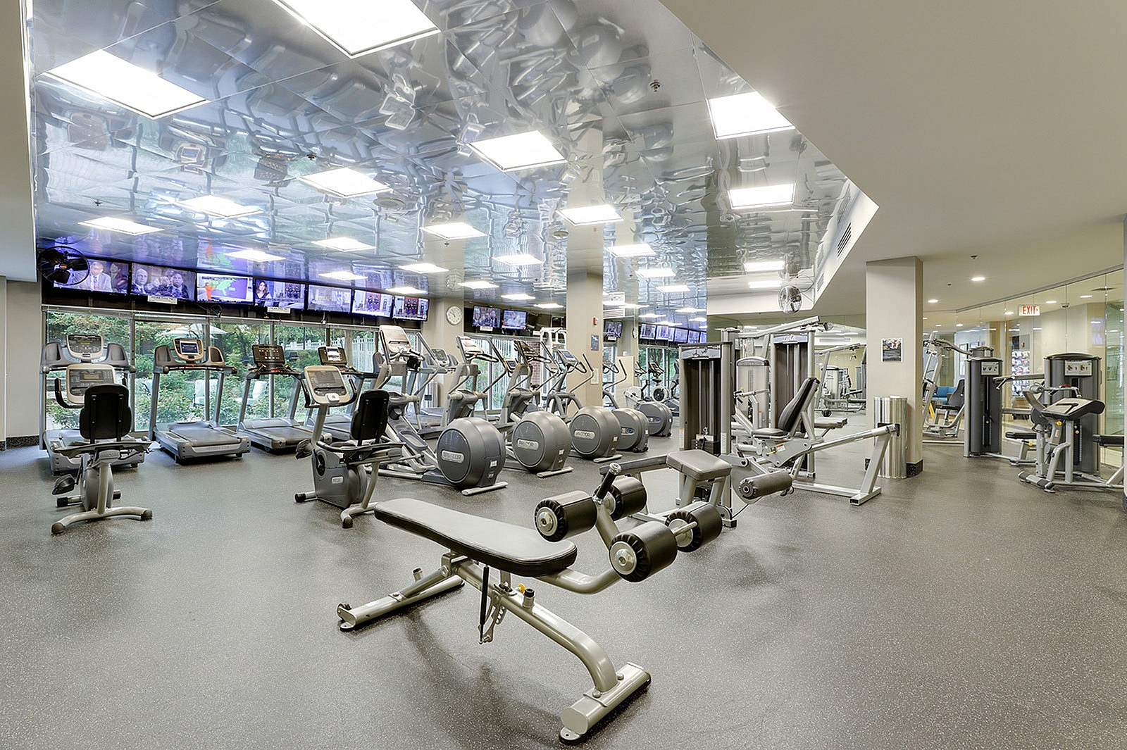 Modern fitness center with state-of-the-art equipment, well-lit interior, and scenic views through large windows.