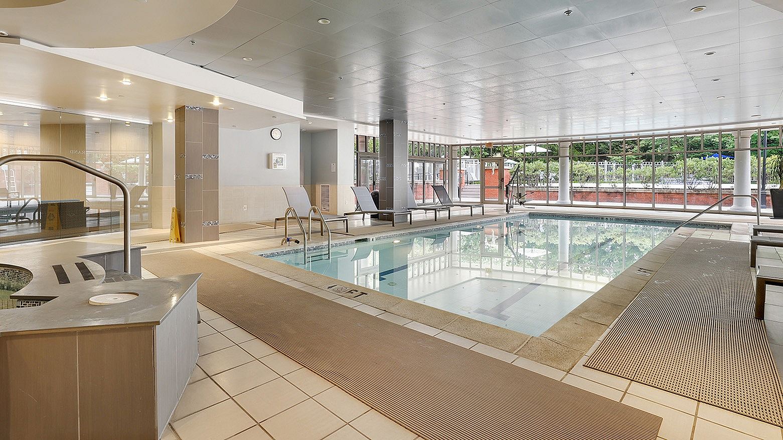 Luxurious indoor pool area with modern lounge chairs and large windows offering scenic views at upscale apartment complex.