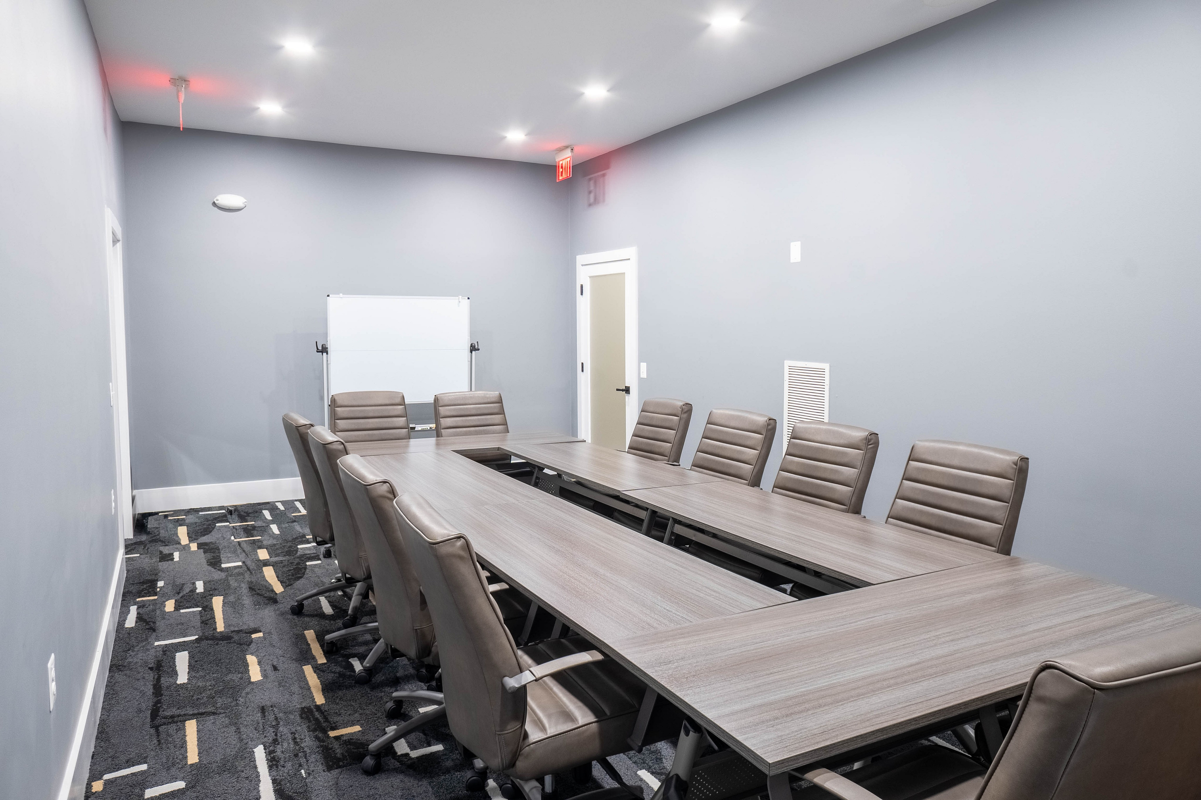 Modern conference room with sleek gray chairs and tables, stylish carpet, and minimalist design, ideal for professional meetings.