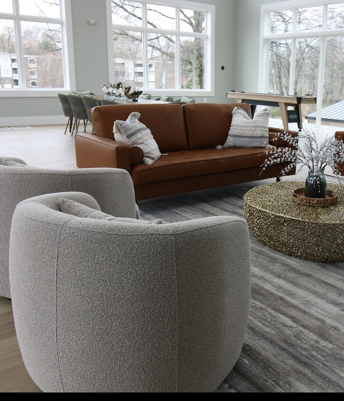 Bright and spacious living room with modern furnishings, featuring leather sofas, cozy armchairs, and a chic coffee table, accentuated by large windows offering scenic views.