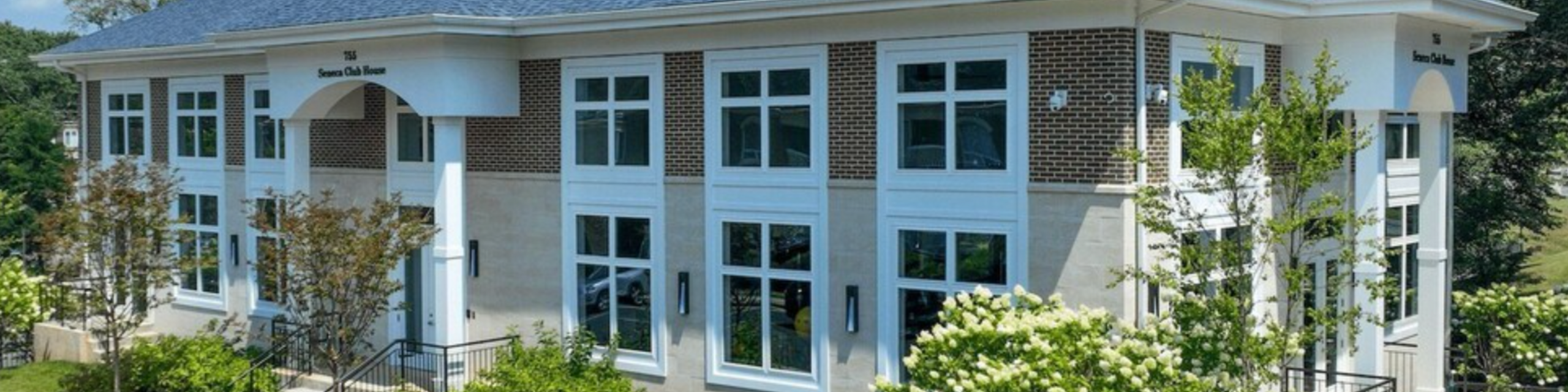Elegant two-story building with modern windows and lush green landscaping, perfect for a vibrant community setting.